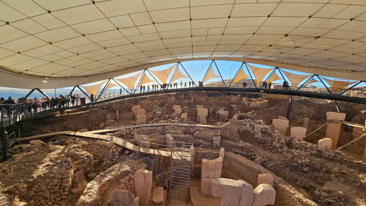 Visitors stand behind a railing and look across the stone excavation area.
