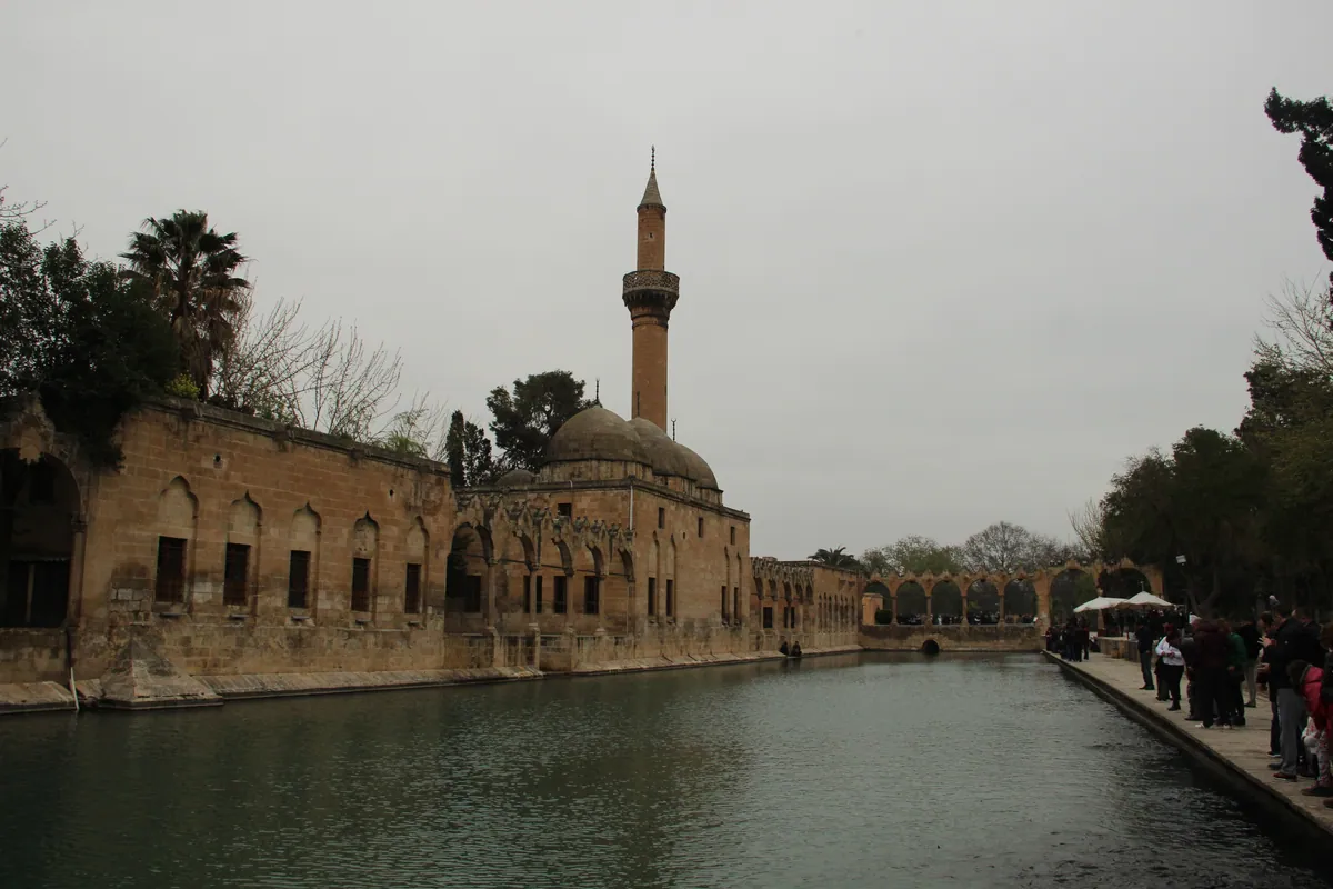 A pond with a stone building and minaret on the opposite bank.