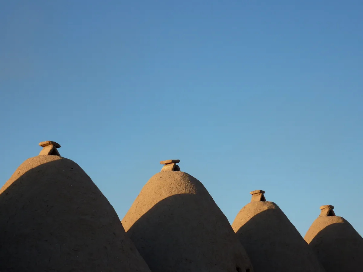 Several low, tan beehive-roof houses against a clear blue sky.