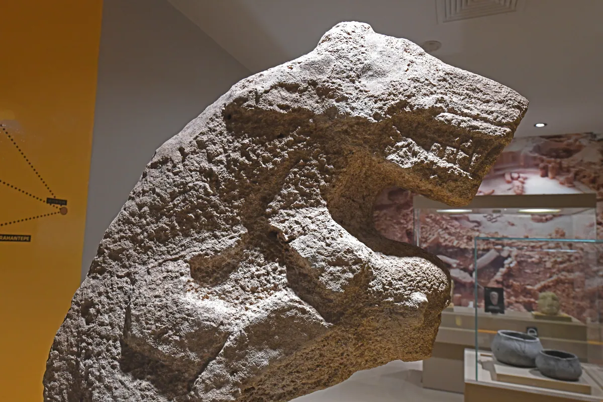 A weathered stone figure of a person bent forward beneath a leopard, shown in close-up.