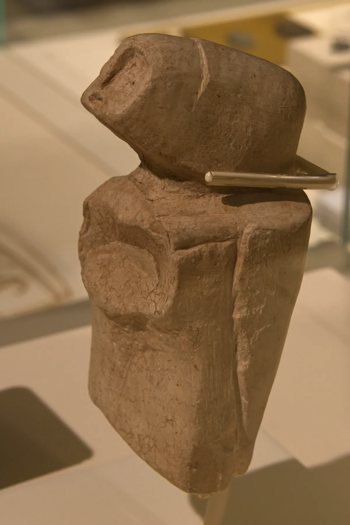 A small stone human figure displayed upright in a glass-lit museum case.